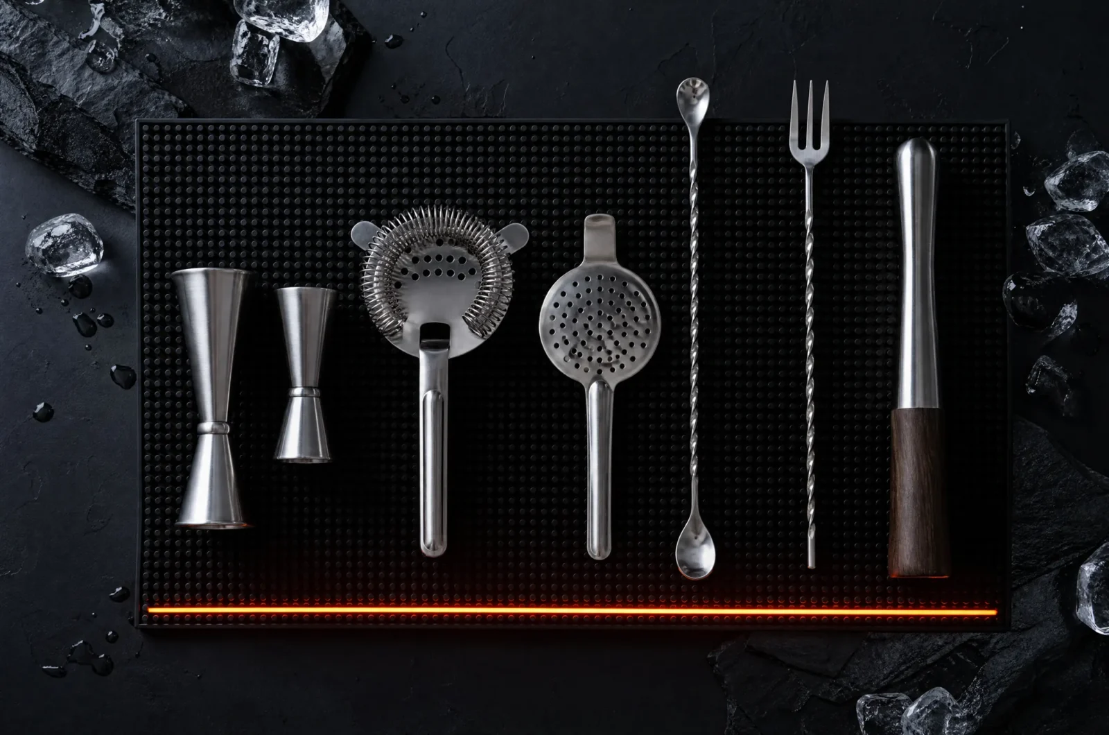 Stainless steel bar tools laid out in parallel on a black silicone bar mat